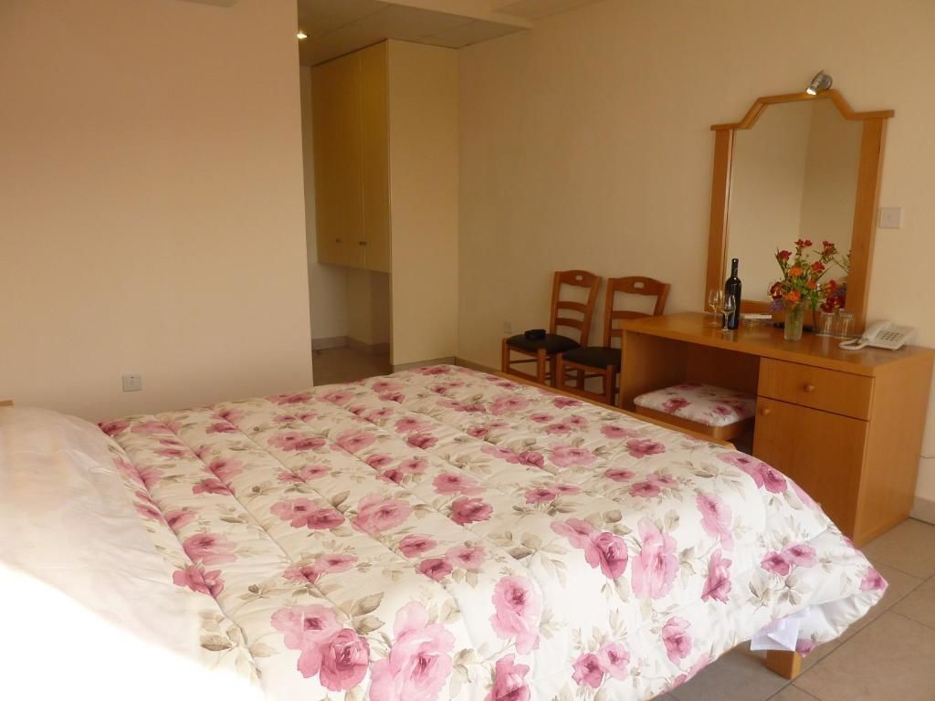 Ein Schlafzimmer mit floralem Bettbezug, einem hölzernen Schminktisch, einem Spiegel und zwei Stühlen.