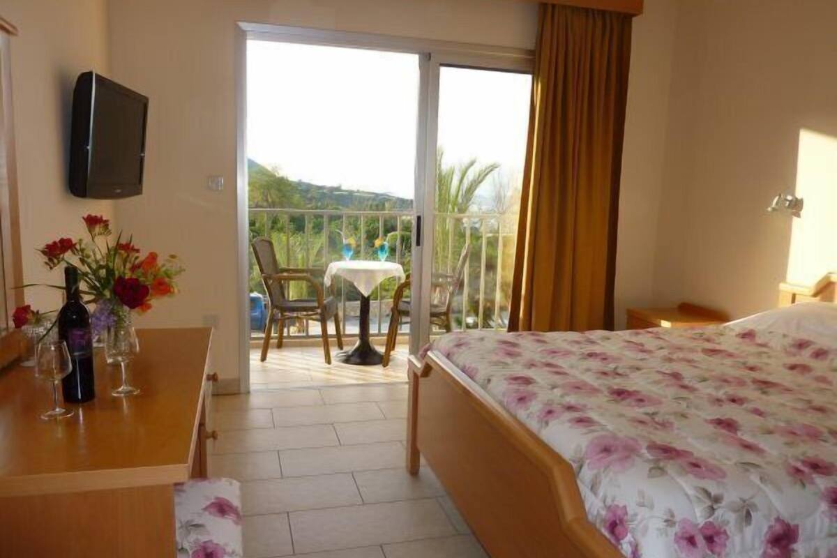 Ein Hotelzimmer mit Bett, einem Balkon mit Tisch und Stühlen sowie einem an der Wand befestigten Fernseher.