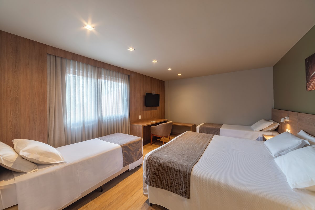 A hotel room with two single beds, a desk, a chair, and a television on the wall.