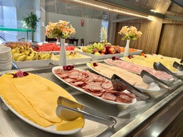 Un bufé con una variedad de alimentos, incluyendo carnes cortadas, quesos, frutas y verduras.