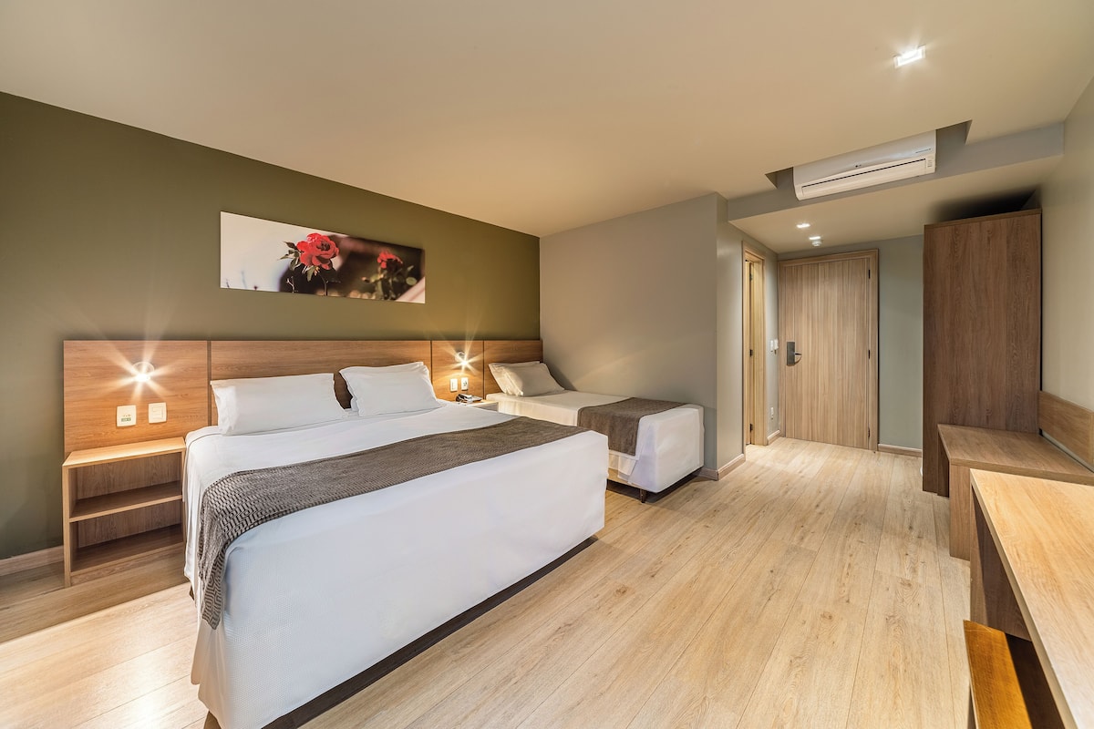 A hotel room with two beds, a wooden headboard, a nightstand, a bedside table, a bench, a wooden floor, and an air conditioning unit.