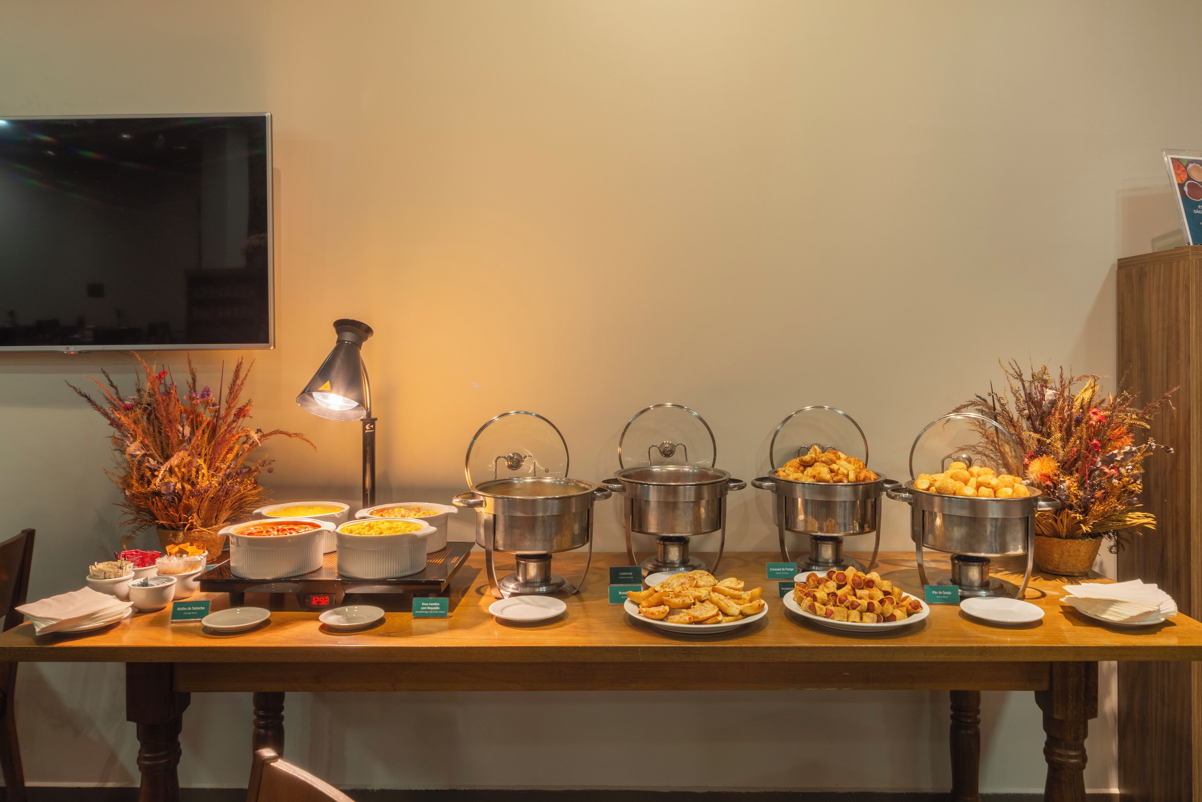 A buffet table with various food items and serving dishes, a lamp, and decorative plants.