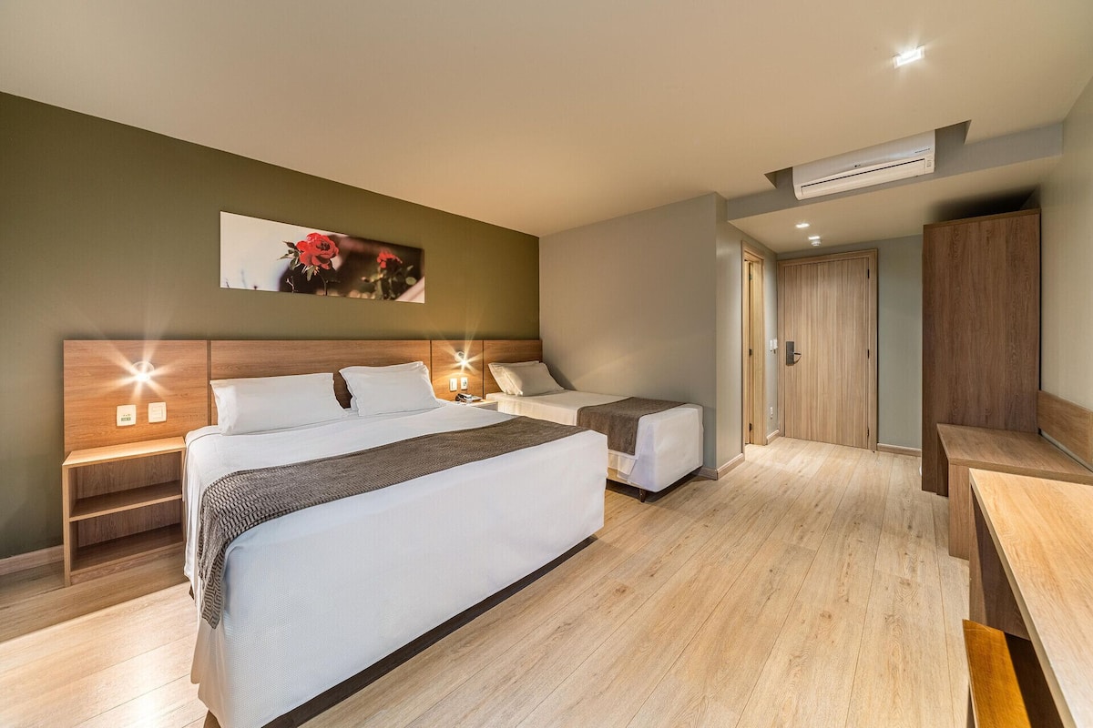 A hotel room with a large bed, bedside tables, a wardrobe, and an air conditioning unit.