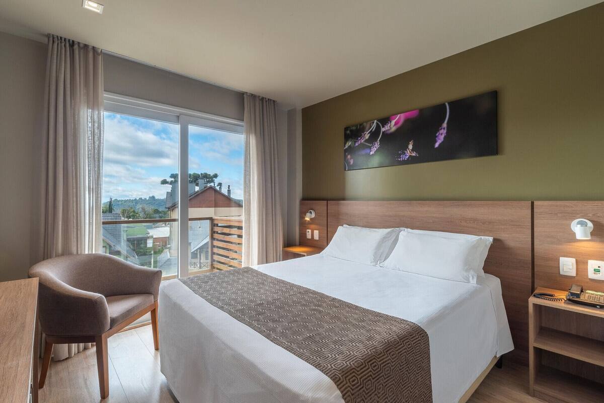 A hotel room with a bed, a desk, a chair, a nightstand, and a painting.