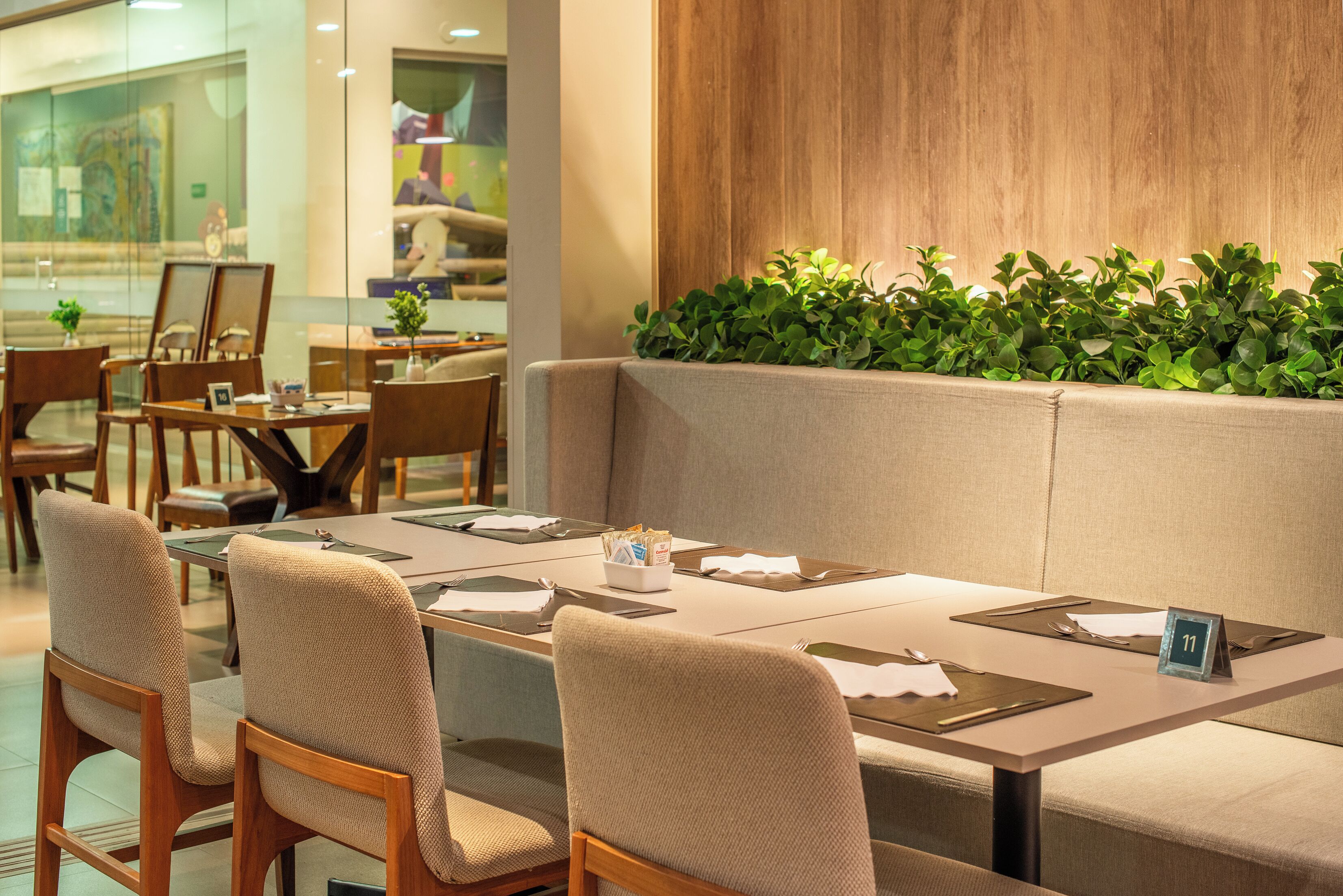 A restaurant with a long table, cushioned seating, and a wooden accent wall.