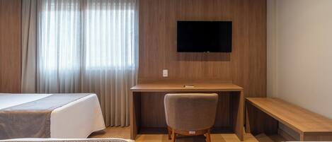 A hotel room with two beds, a desk, a chair, a TV mounted on the wall, and a large window with curtains.