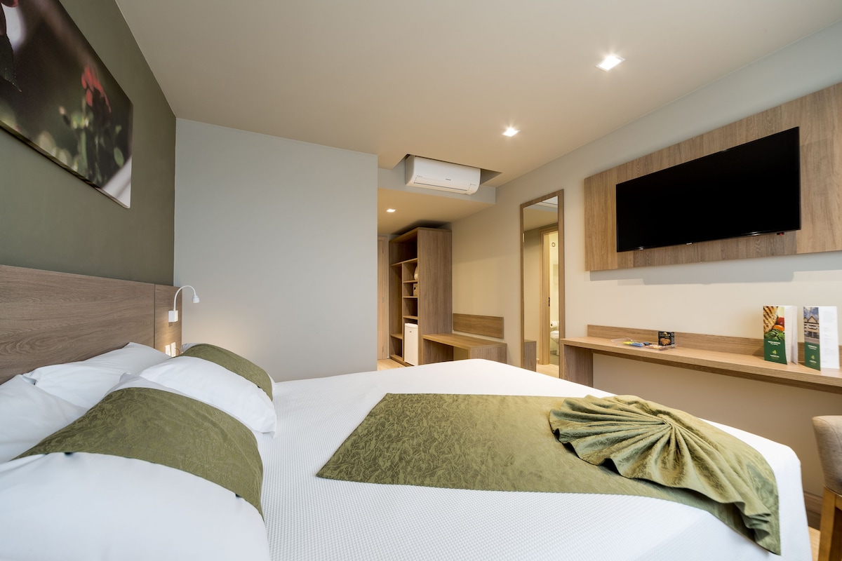 A hotel room with a bed, a TV mounted on the wall, and a closet.