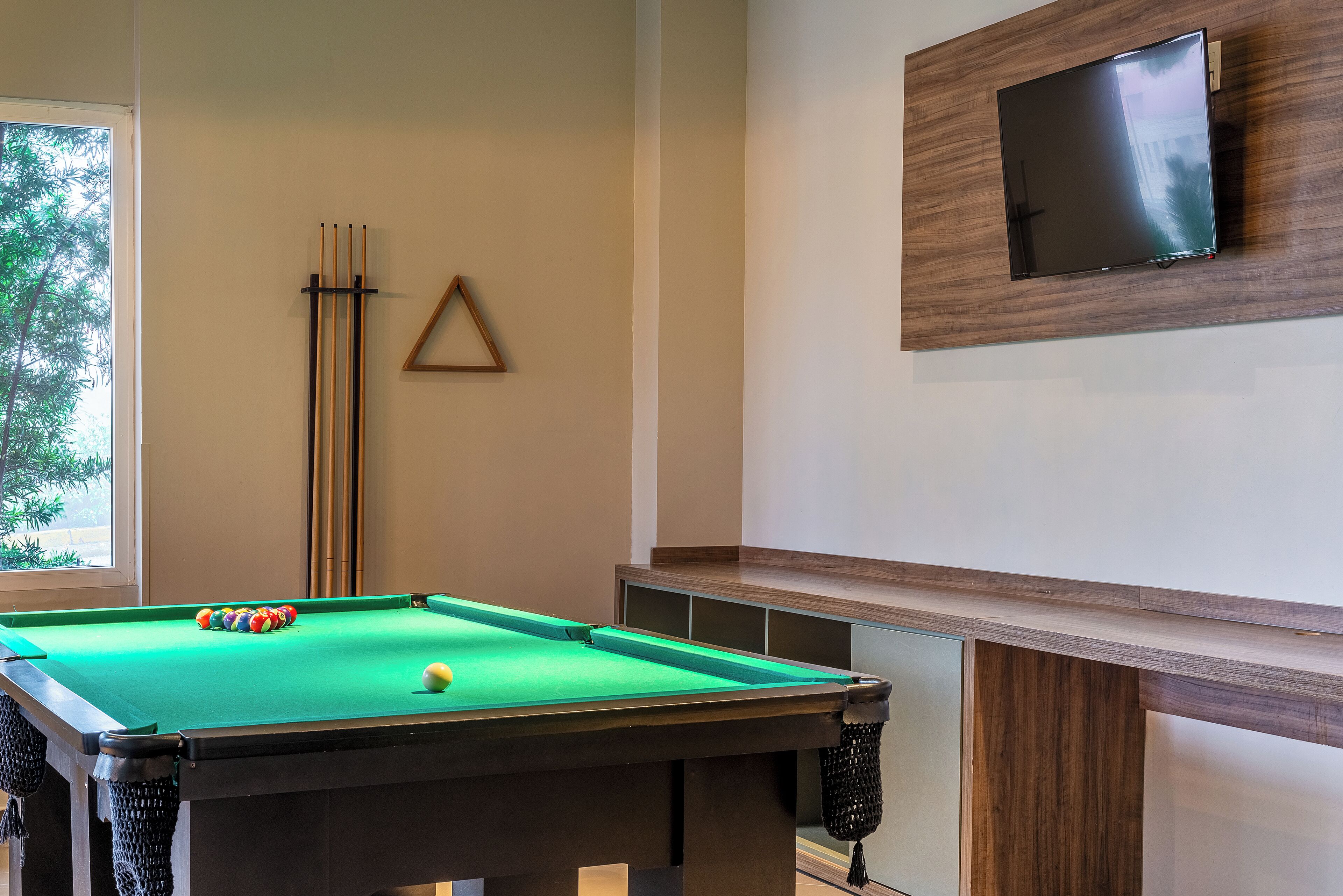 A pool table with balls, a pool cue rack, and a TV mounted on the wall.