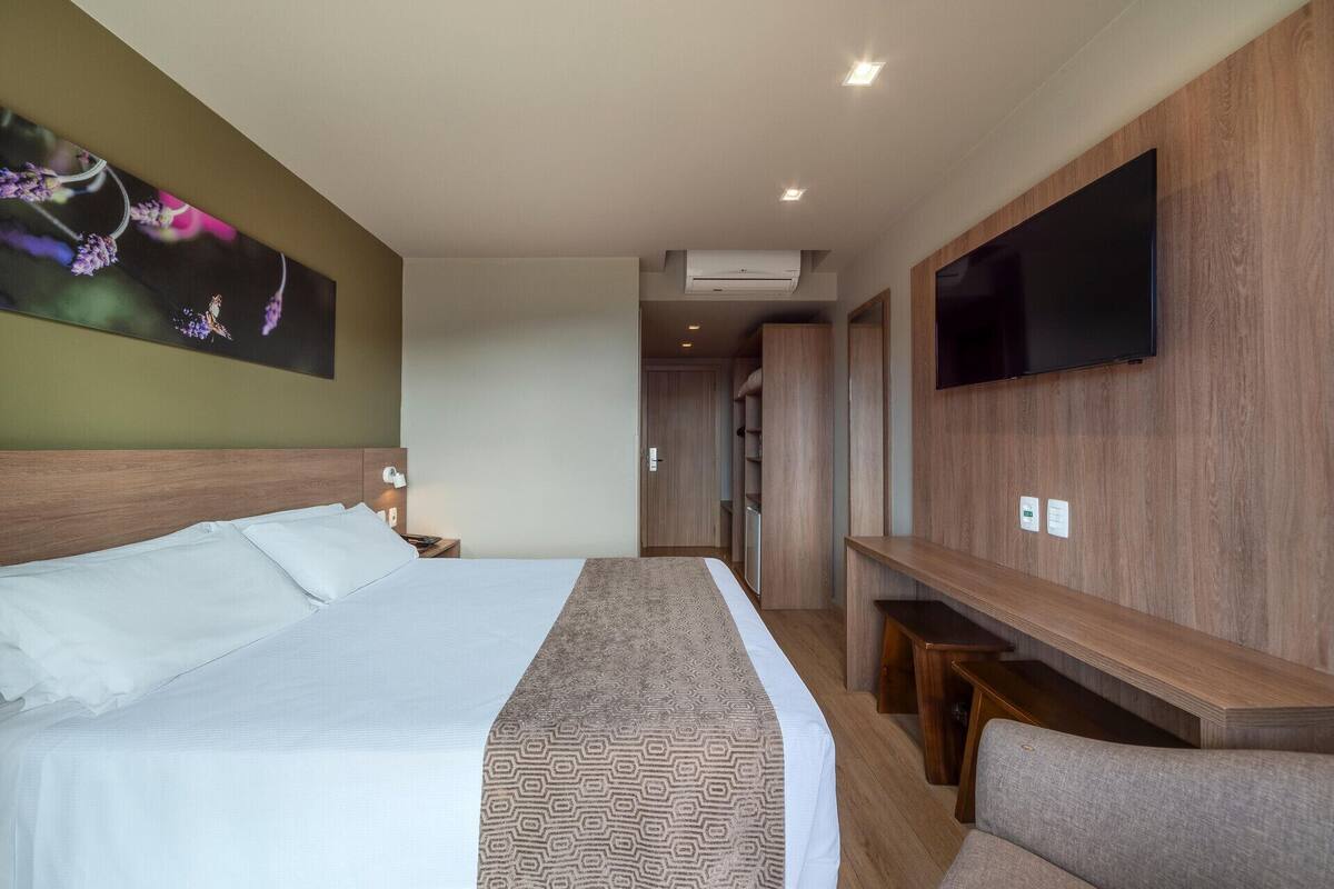 Ein Hotelzimmer mit Bett, Fernseher, Schreibtisch und Stuhl.