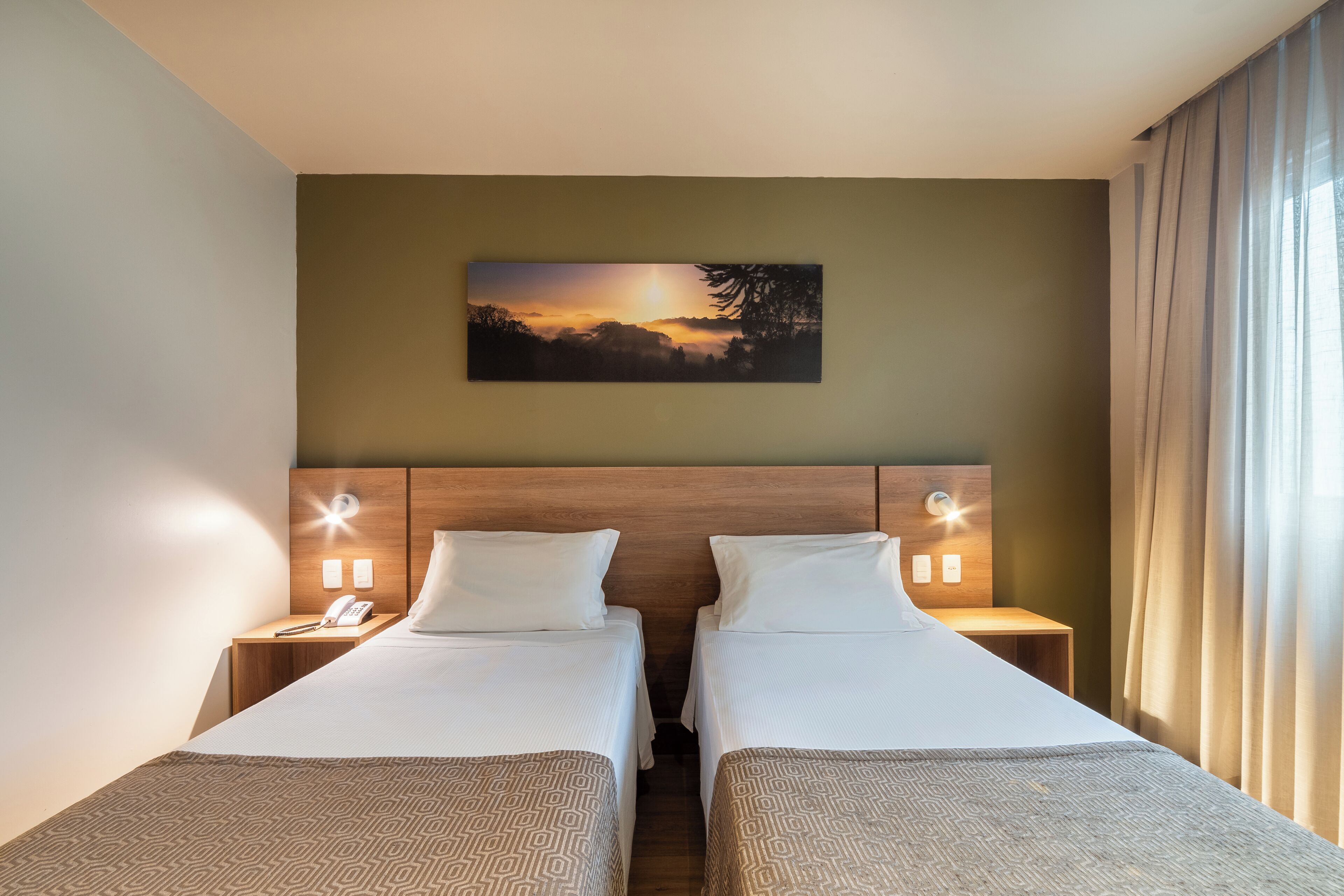 A hotel room with two beds, a headboard with built-in lighting, a painting above the beds, and a nightstand with a phone and lamp.