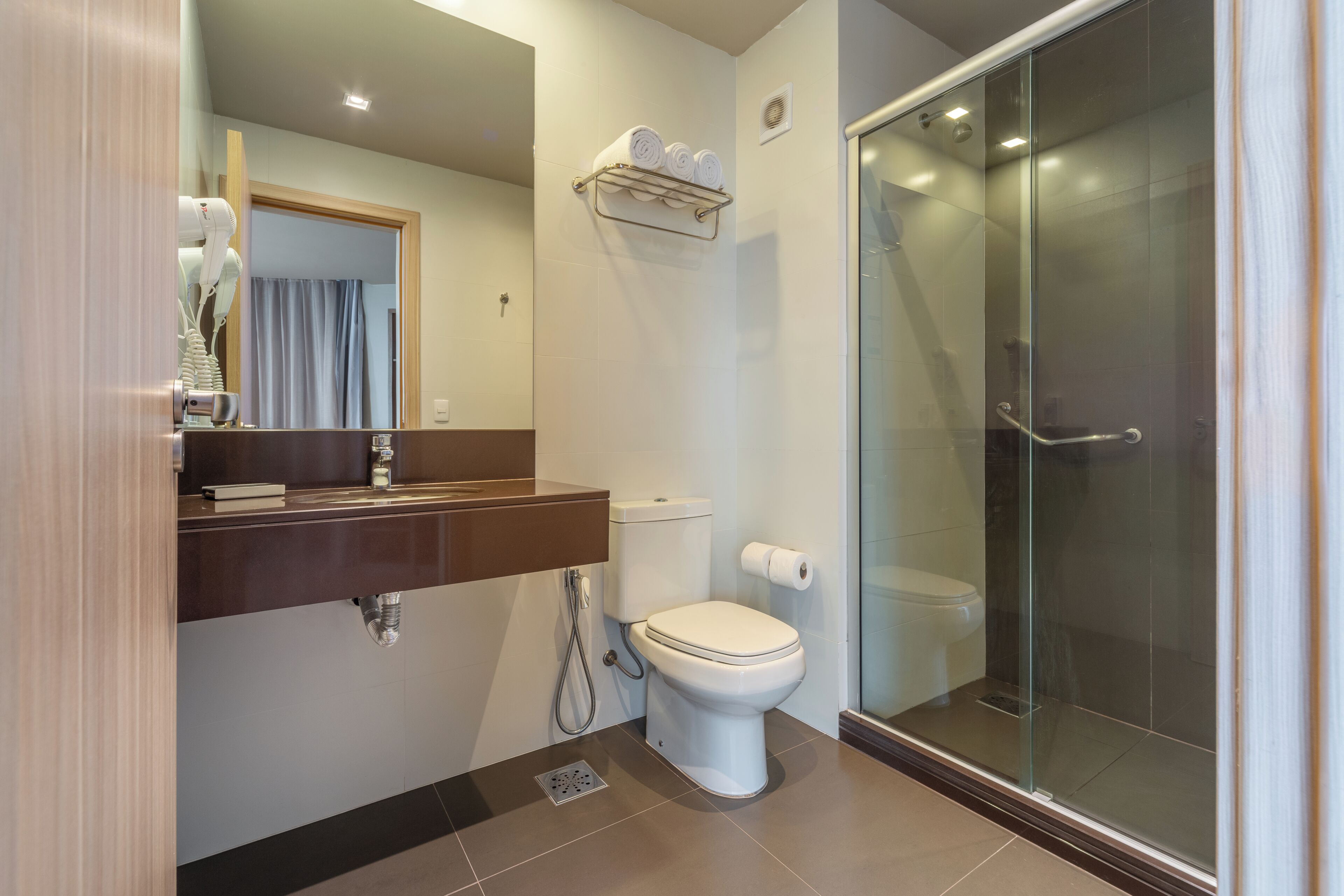 A modern bathroom with a toilet, a shower, a sink with a mirror, and a towel rack.