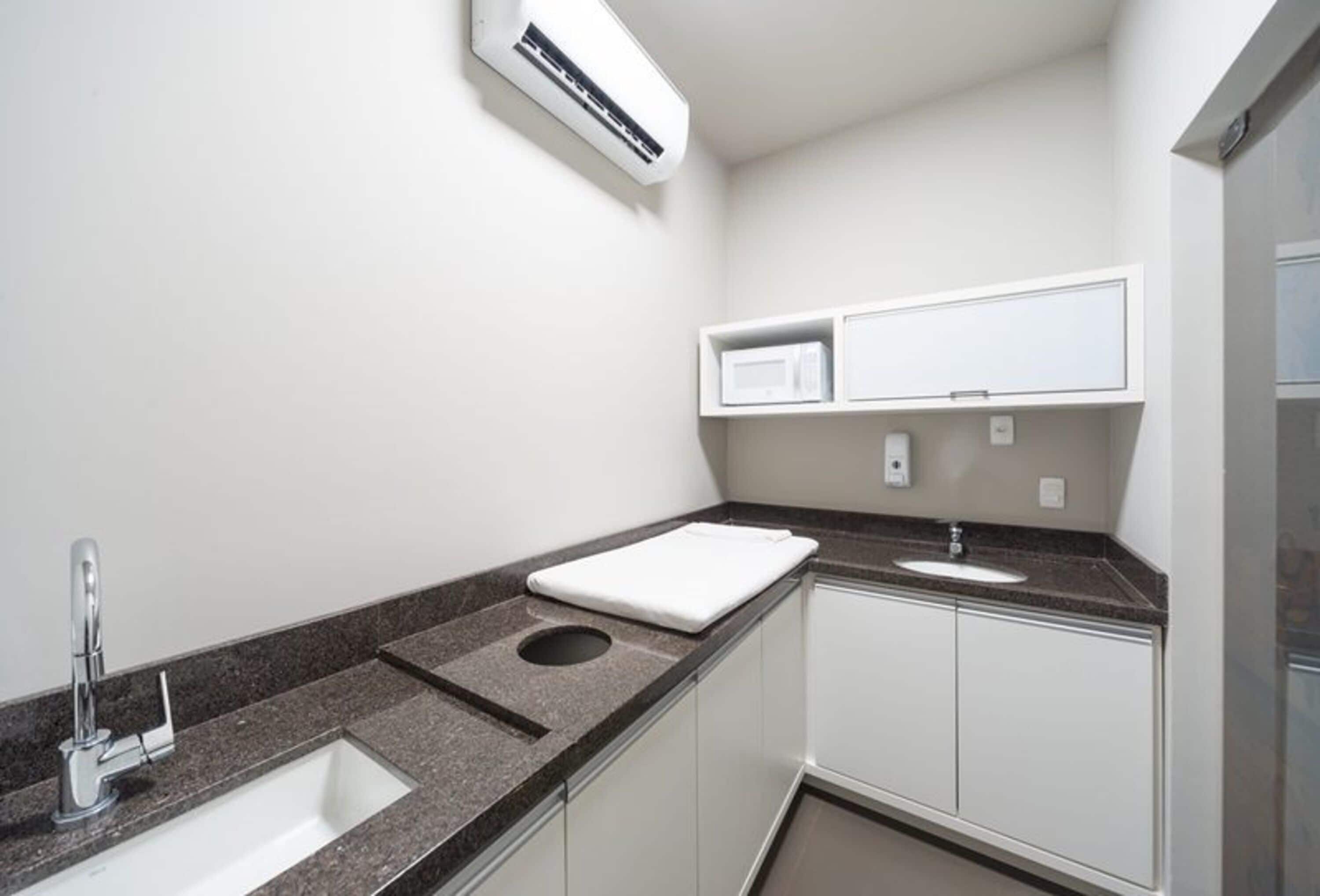 A compact bathroom with a sink, a mirror, a towel, and a microwave.