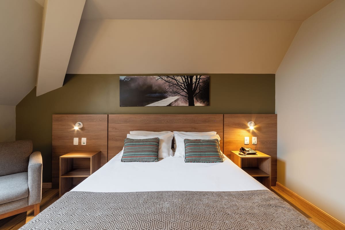 A modern hotel room with a large bed, two bedside tables, a nightstand, a chair, and a painting on the wall.