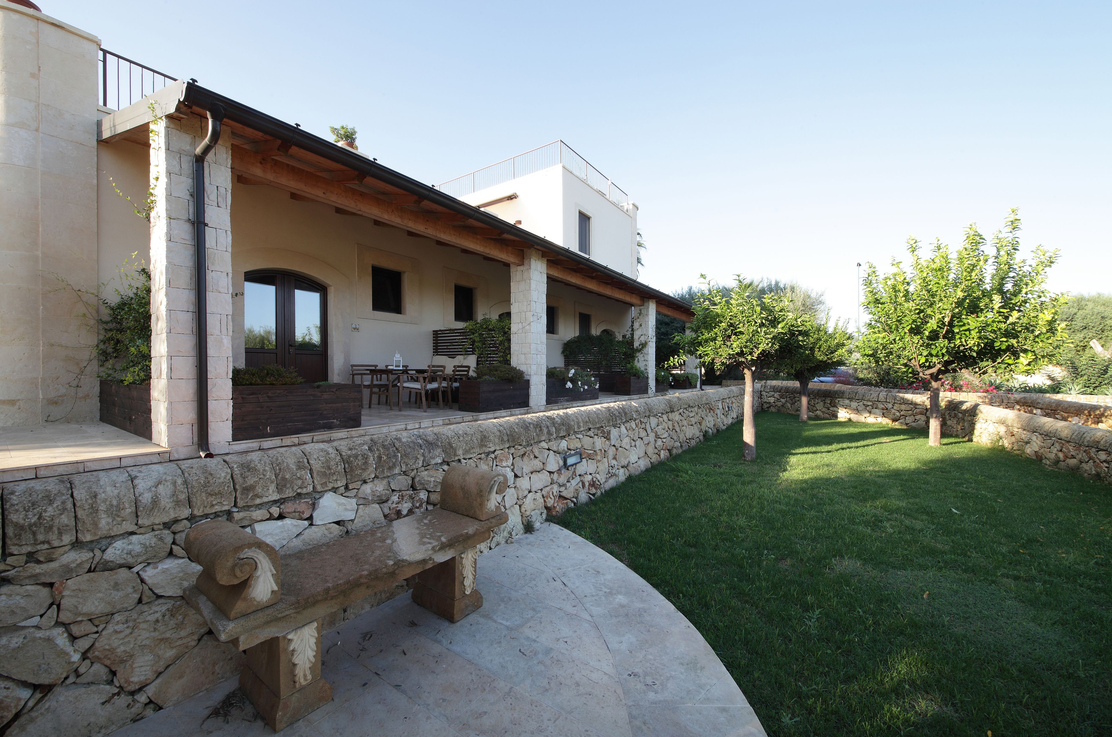 Une maison moderne avec un mur en pierre, un banc en bois et une pelouse bien entretenue.