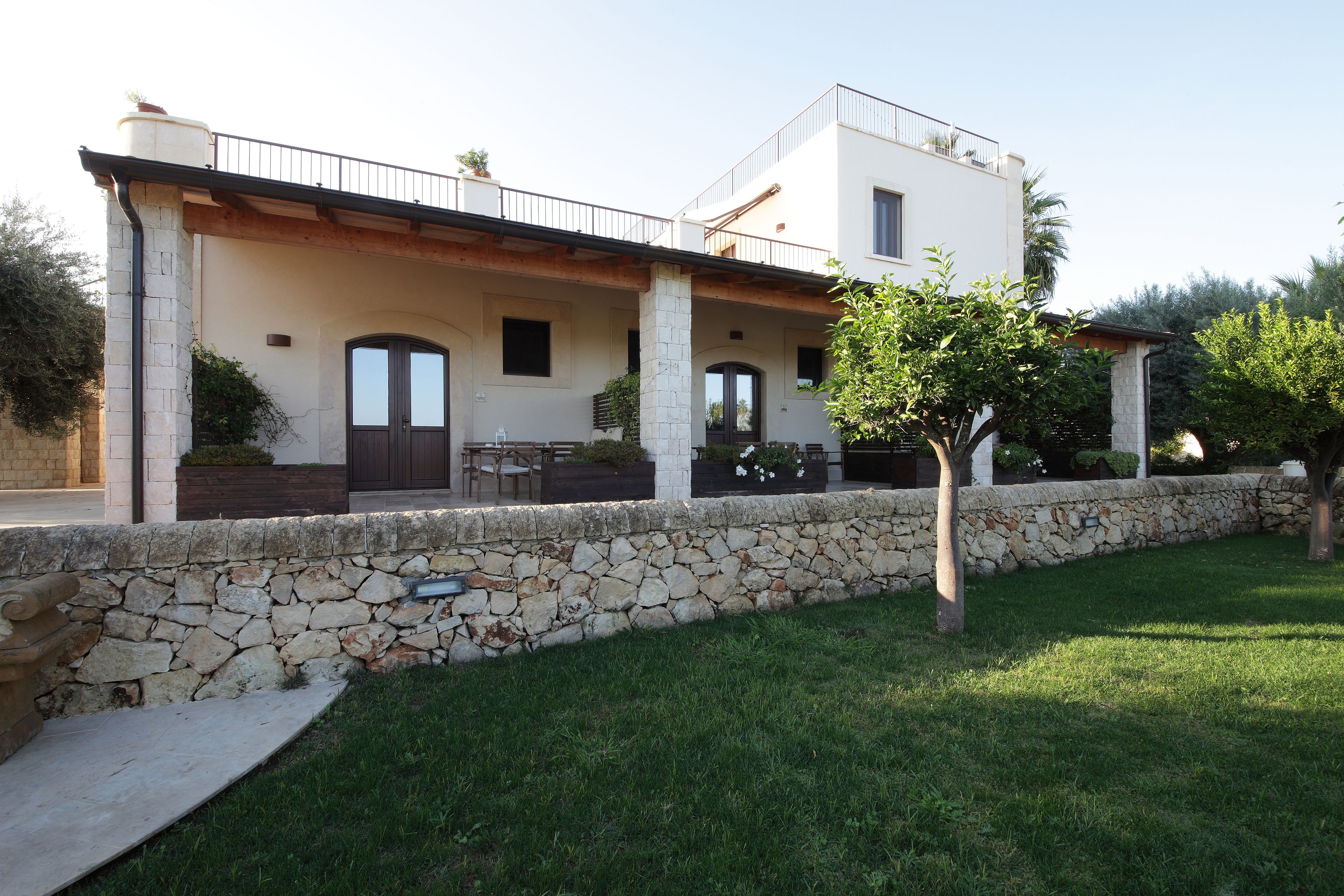 A two-story house with a stone foundation, a balcony with a metal railing, and a well-maintained lawn.