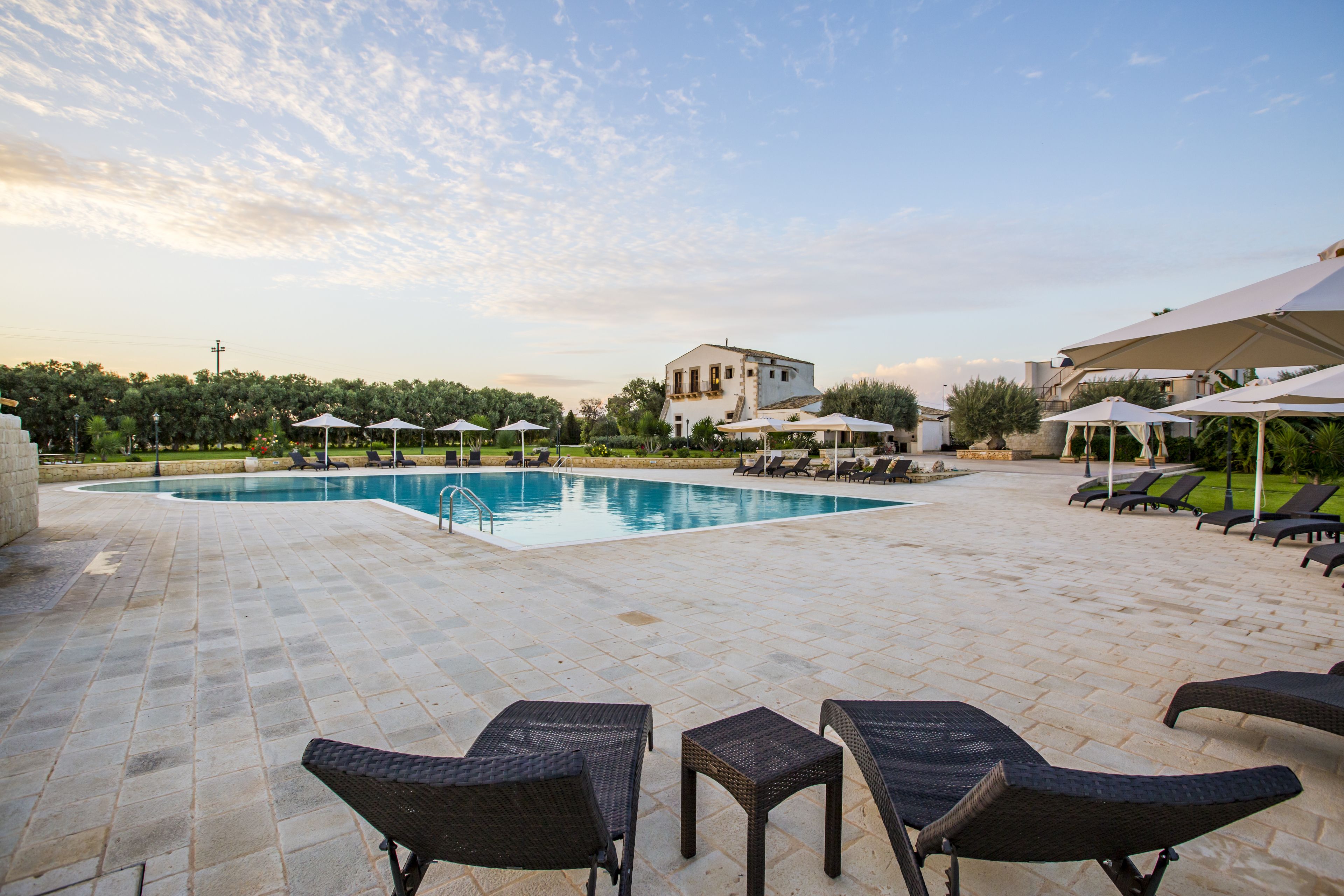A pool area with lounge chairs, umbrellas, and a building in the background.