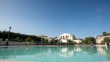 Una piscina al aire libre, sombrillas, sillones reclinables de piscina