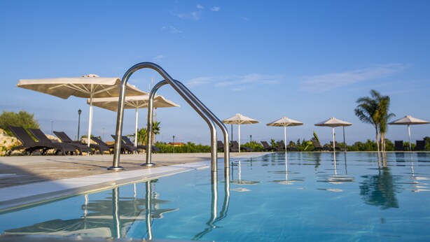 Una piscina con sillas de descanso y sombrillas, rodeada de palmeras.