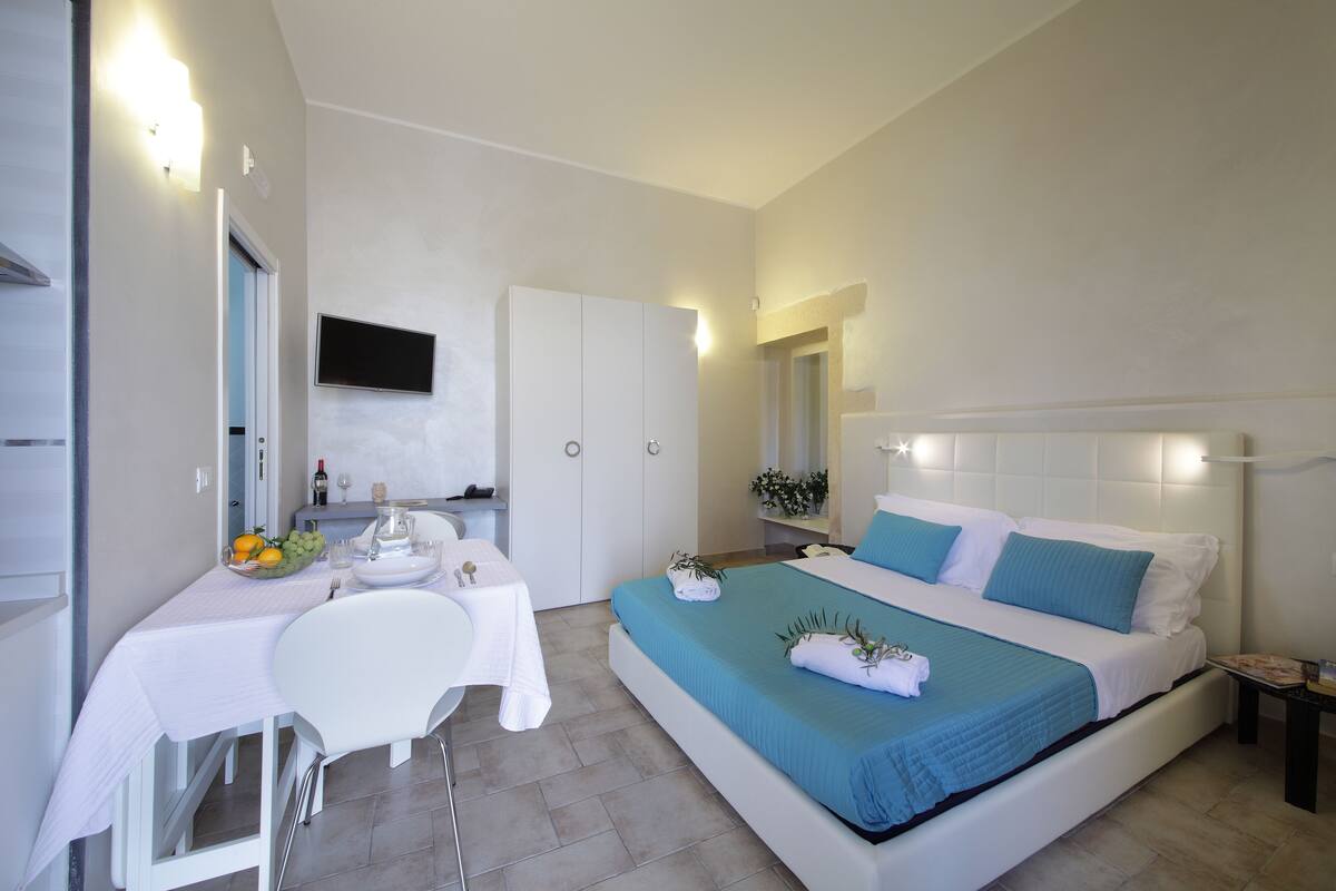 A bedroom with a bed, a desk, a chair, and a TV mounted on the wall.