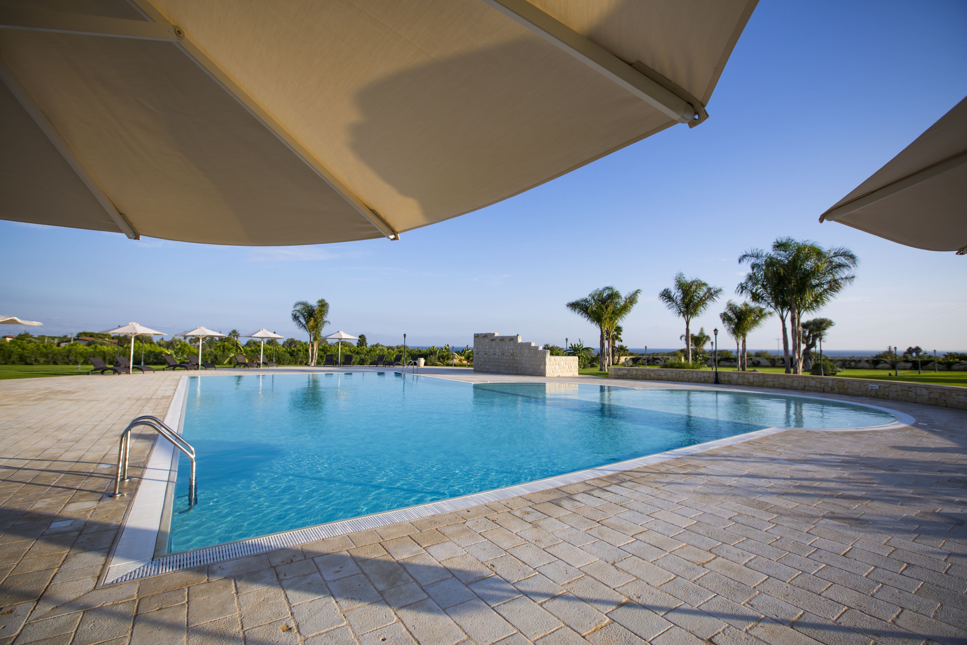 Piscina con borde de piedra, rodeada de sombrillas y palmeras.