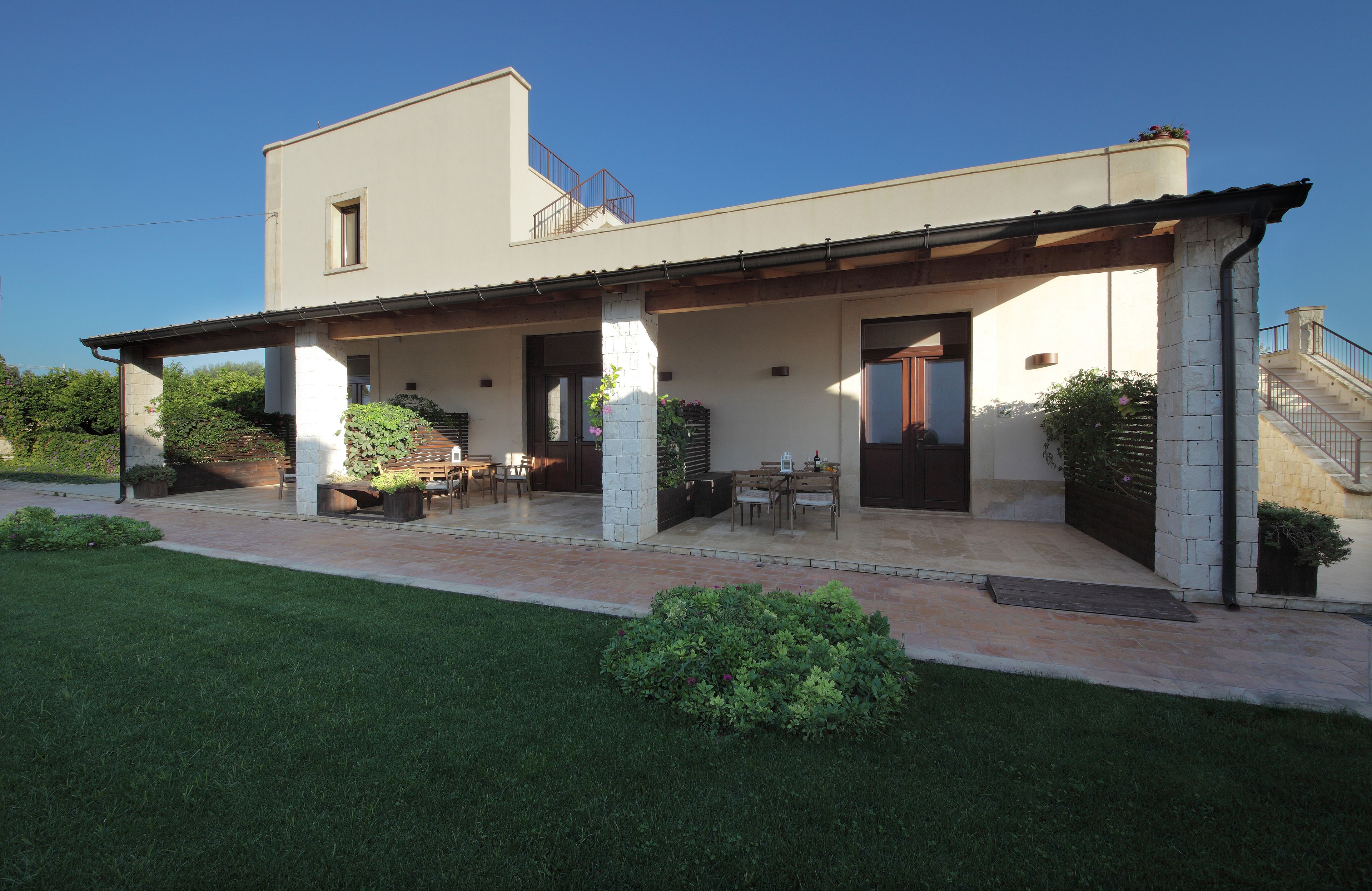 Una casa de dos pisos con un porche cubierto, mobiliario para exterior y una escalera que conduce al piso superior.