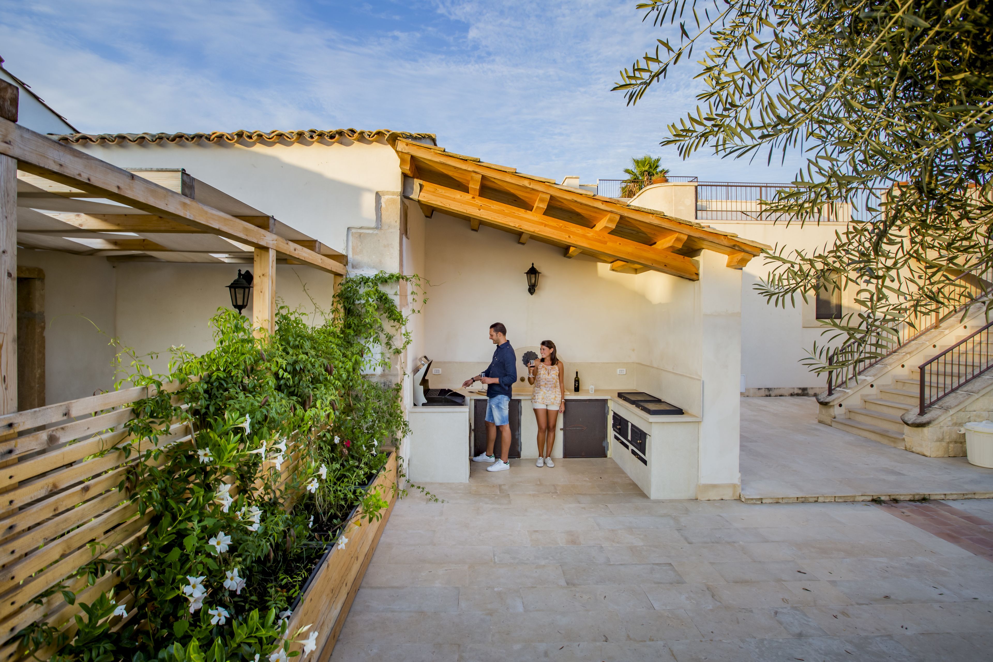 Eine Terrasse mit einer Pergola, einer kleinen Küche und einer hölzernen Bank.