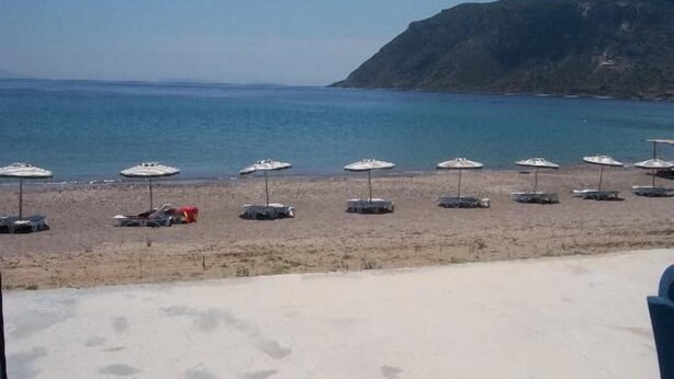 A beach with umbrellas and lounge chairs, a clear view of the sea, and a rocky hill in the background. - Christina Studios (Kos)