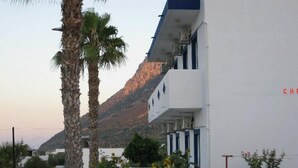 A white building with blue accents, a mountain in the background, and palm trees in the foreground. - Christina Studios (Kos)