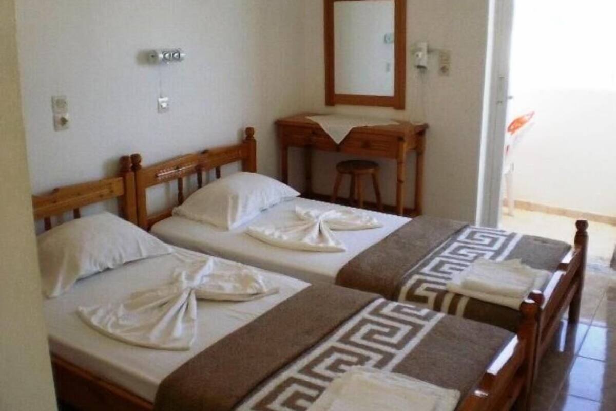 A hotel room with two wooden beds, a wooden desk, a mirror, and a small stool.