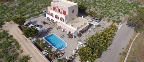 Vista aérea de un hotel con piscina, varias edificaciones y vegetación circundante.