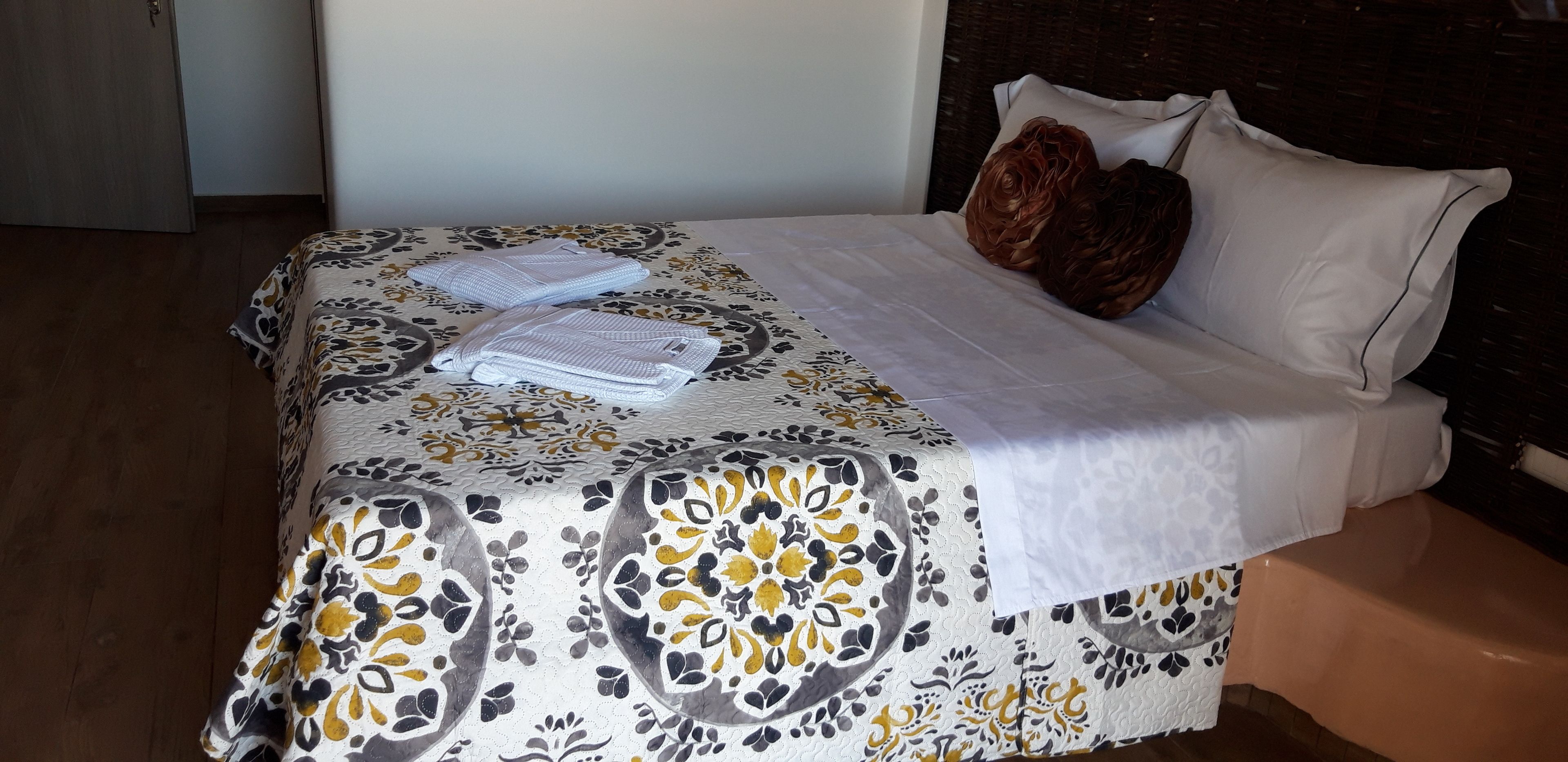 A neatly made bed with a patterned bedspread, two folded towels, and decorative pillows.