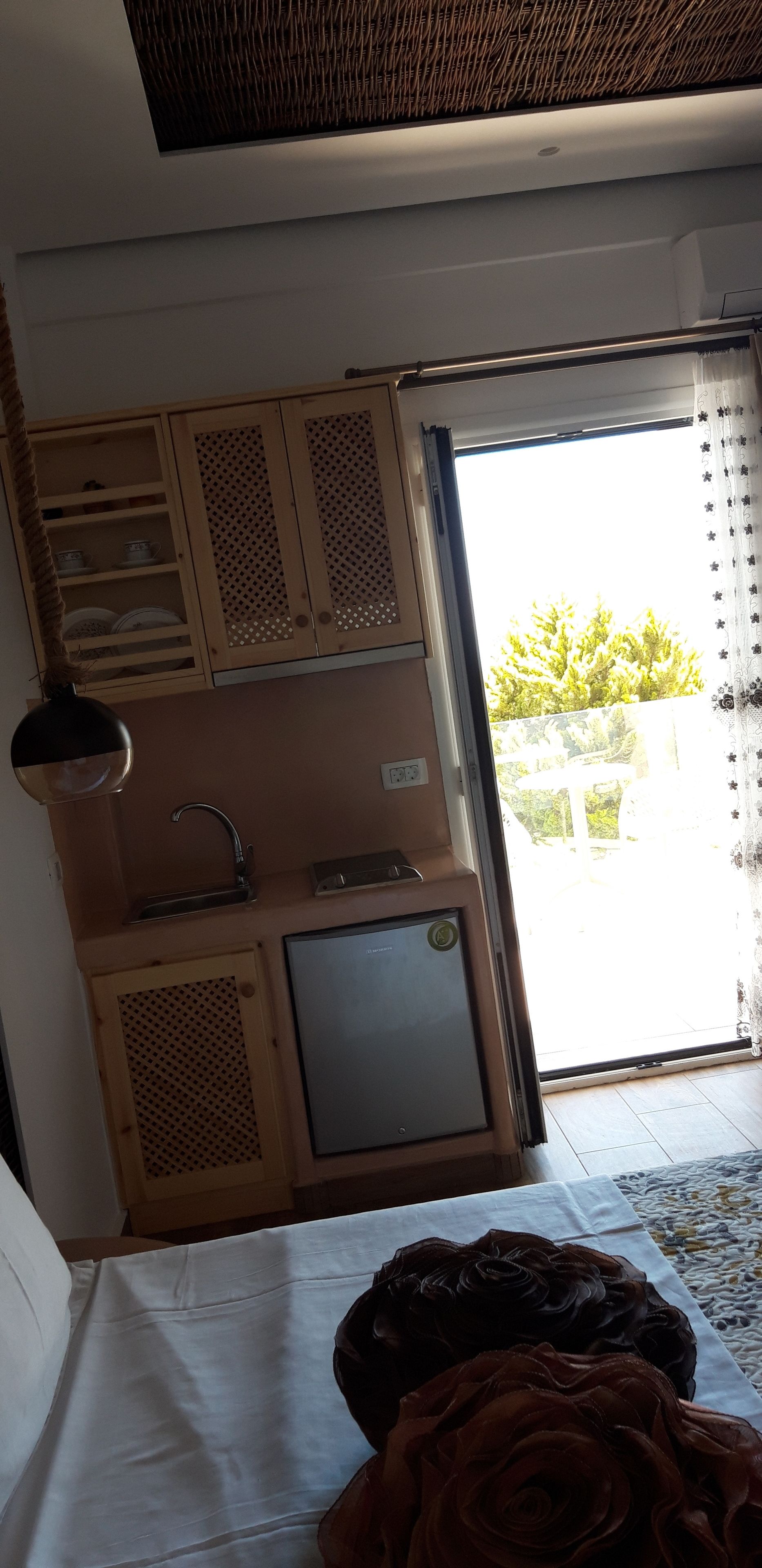 A room with a kitchenette, a small refrigerator, a sink, and a window with a view of greenery outside.