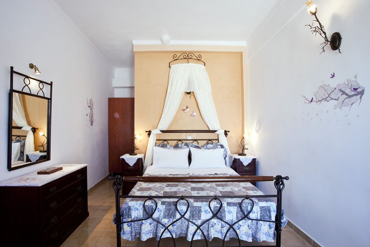 A bedroom with a canopy bed, a bedside table with a lamp, a dresser, and a wall with a floral mural.