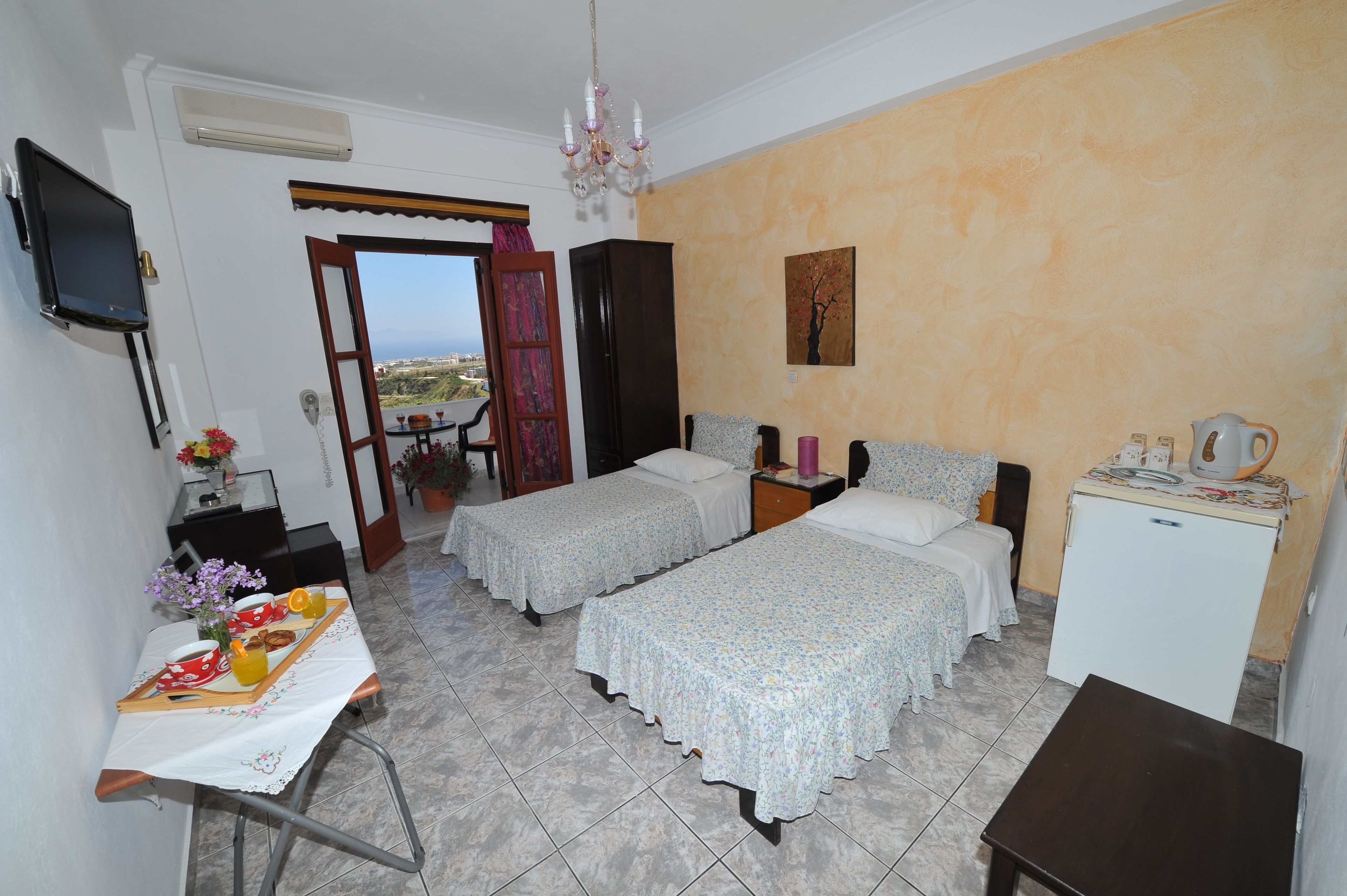 A hotel room with two beds, a desk with a tray of breakfast, a TV, and a view of the outdoors.