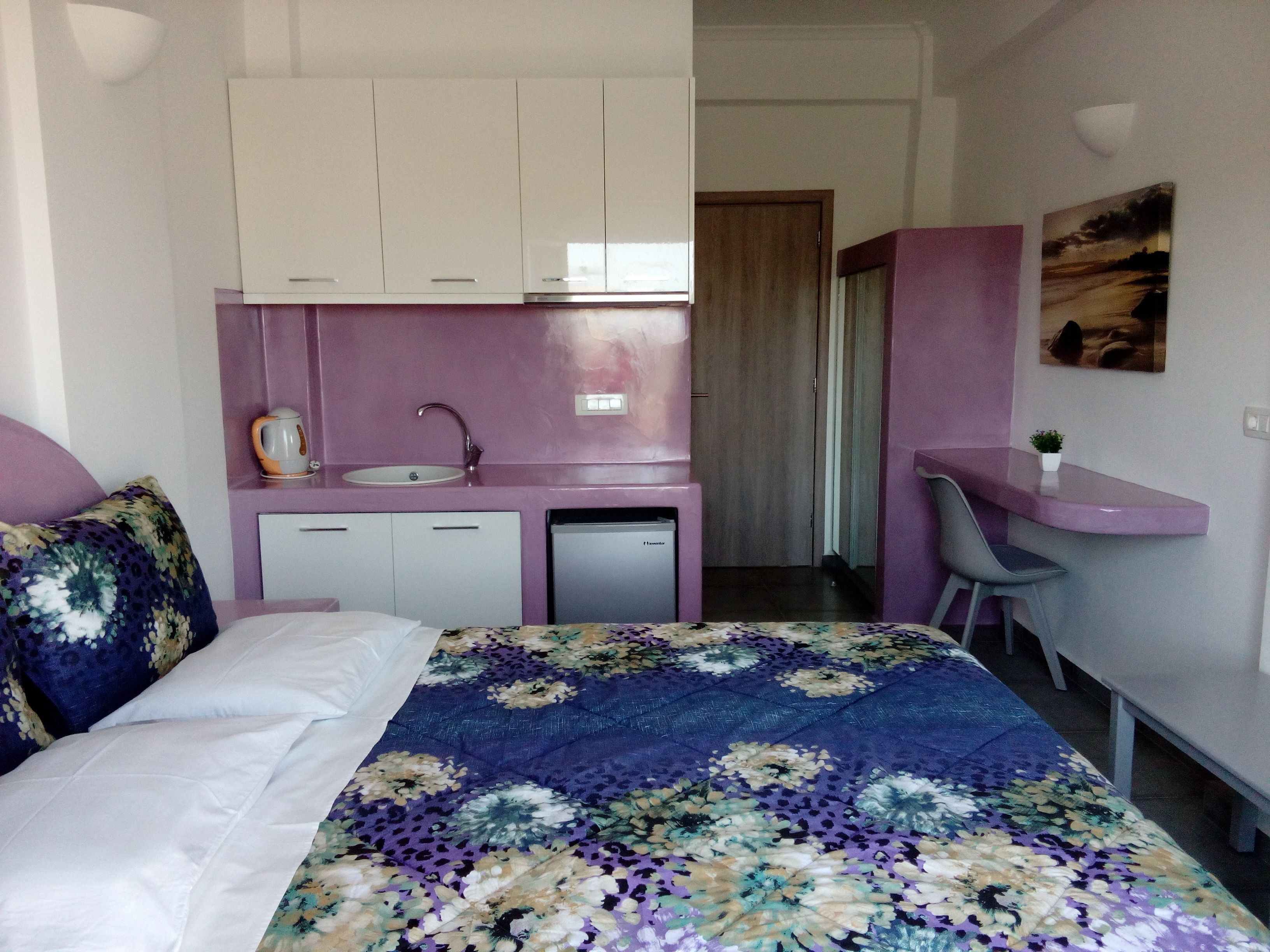 A bedroom with a bed, a desk, a sink, and a small kitchenette.