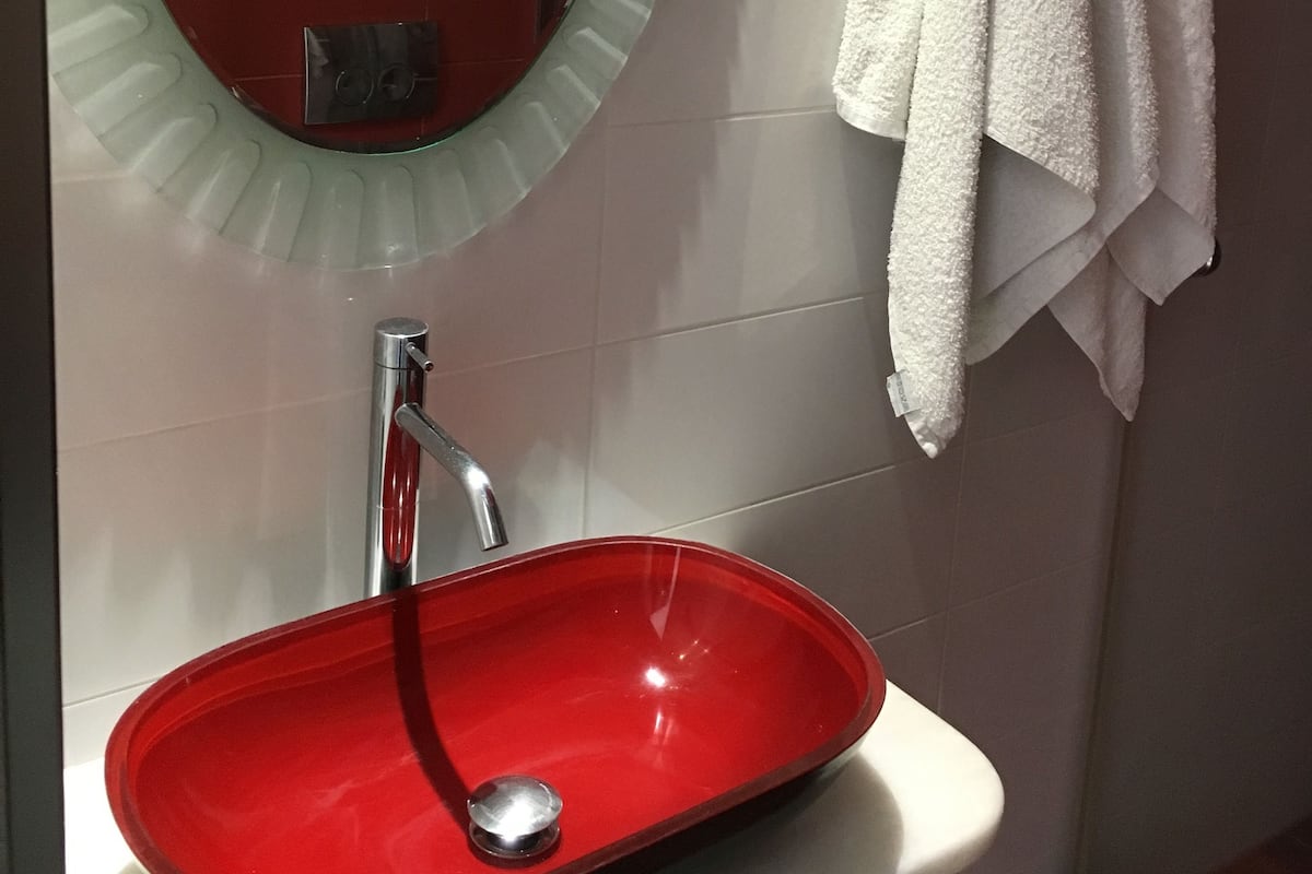 A bathroom with a red sink, a mirror, and a towel rack with white towels.