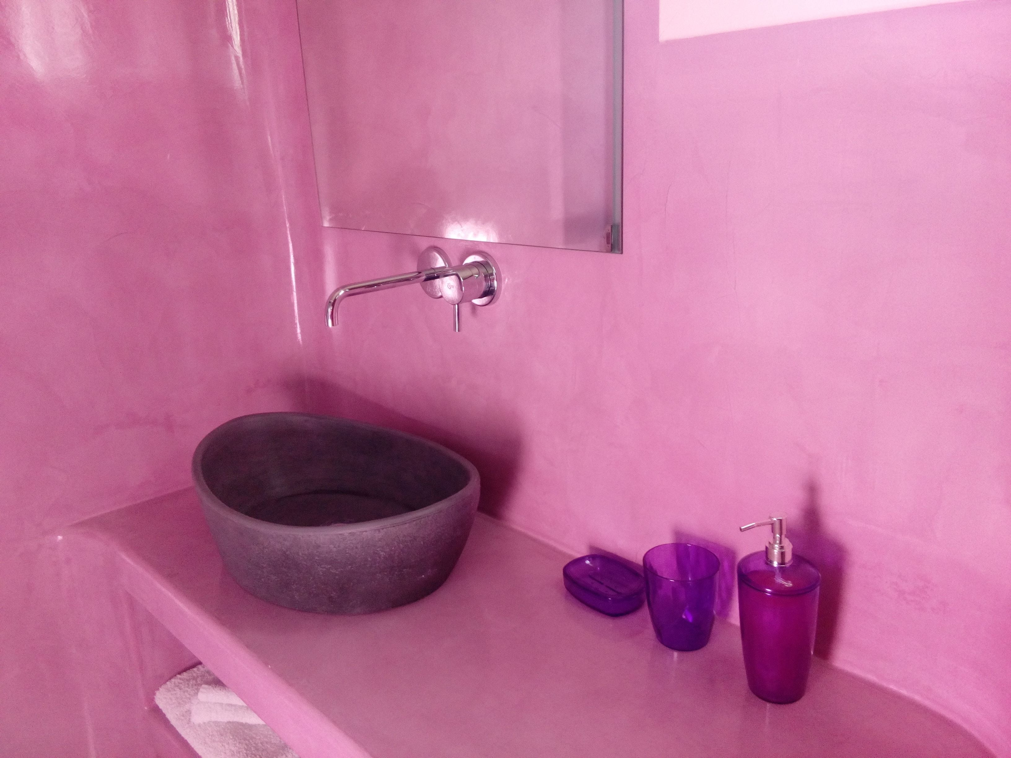 A bathroom with a pink wall, a round basin, and two purple bottles.