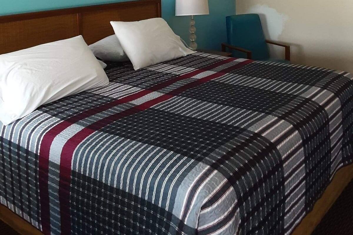 A hotel room with a bed, a nightstand, a lamp, and a wall with three framed pictures.