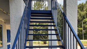 Una scala di metallo blu che conduce a una zona esterna con vista su alberi e cielo sereno.