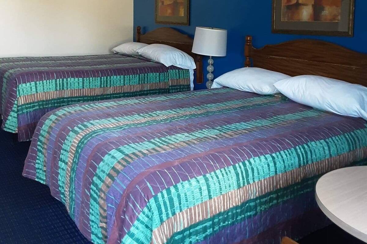 A hotel room with two beds, a round table, and two paintings on the walls.