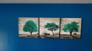 Un letto con una coperta a quadri, due cuscini bianchi e tre quadri con paesaggi su una parete blu.