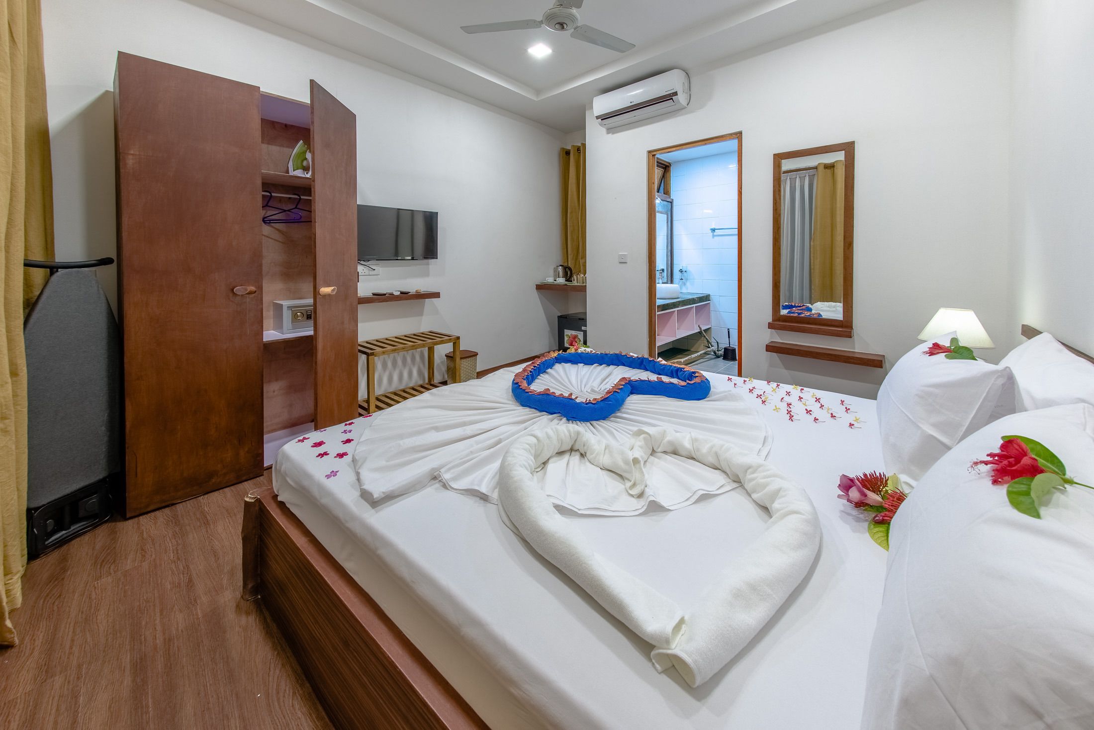 A hotel room with a neatly made bed, a wardrobe, a television, and a mirror.