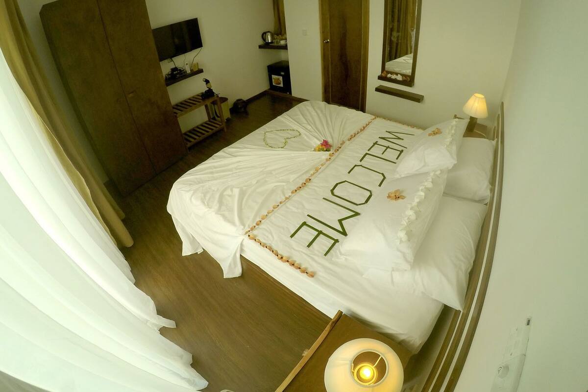 A hotel room with a bed, a television, a wardrobe, a mirror, and a bedside table with a lamp.