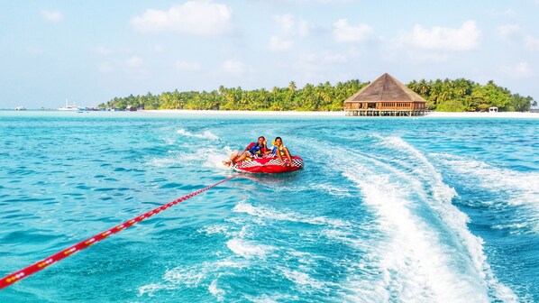 A couple on a jet ski in turquoise waters with a thatched-roof structure in the background.