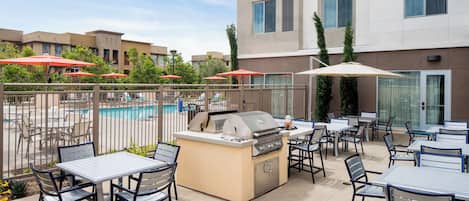 An outdoor patio with tables and chairs, a barbecue grill, and a swimming pool.