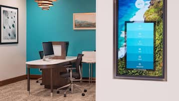 A conference room with a desktop computer, a modern pendant light, and a framed artwork on the wall.