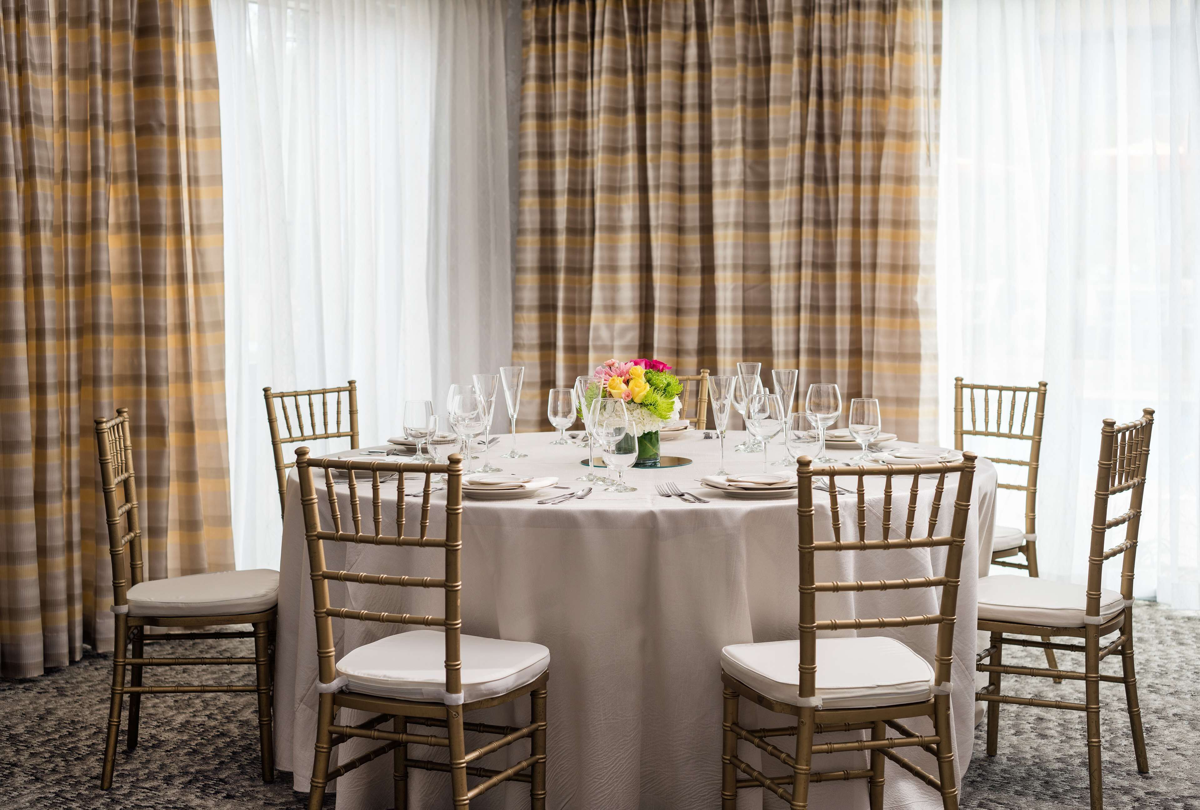 A round dining table with white tablecloth, six chairs, and a vase with flowers.