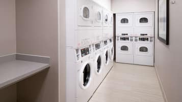 A laundry room with multiple washing machines and dryers, a grey countertop, and a tiled floor.