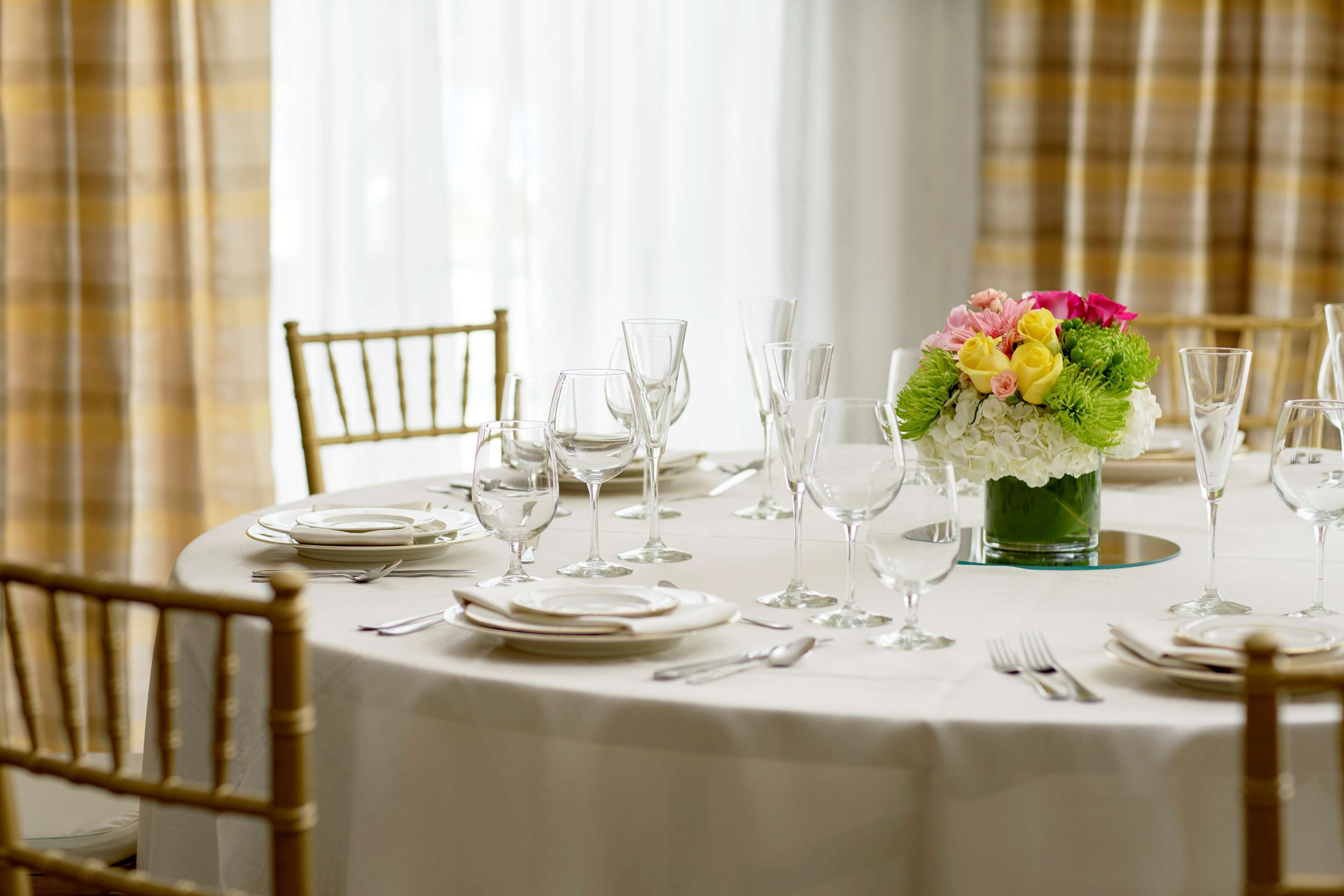 A round dining table set with white tablecloth, plates, glasses, and cutlery. A vase with flowers is placed in the center.
