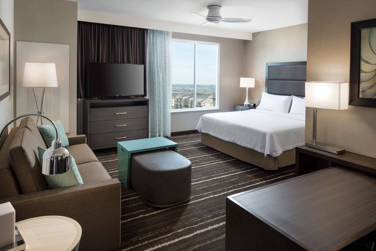 A hotel room with a bed, a TV, a desk, a sofa, and a view of the city.